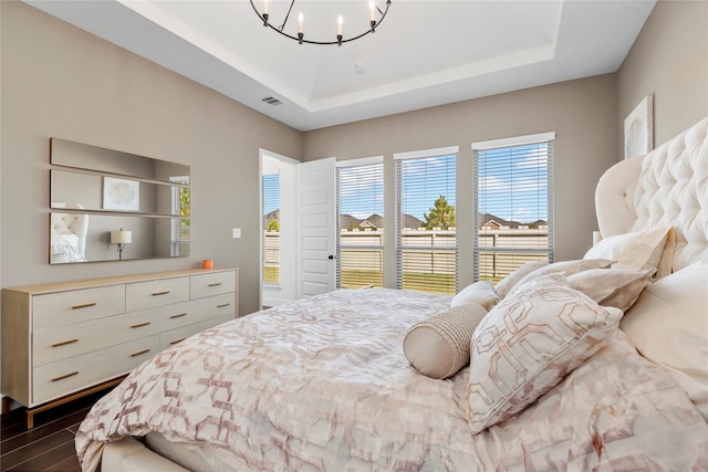 bedroom featuring a tray ceiling, an inviting chandelier, and dark wood-type flooring