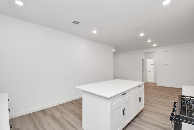 kitchen featuring gas range oven, a center island, light hardwood / wood-style flooring, and white cabinetry