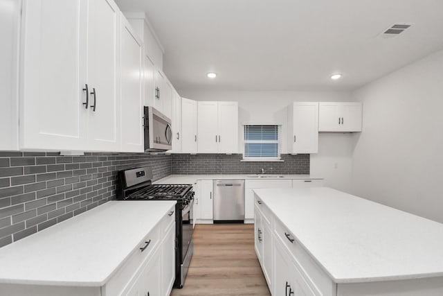 kitchen with white cabinets, a kitchen island, backsplash, and appliances with stainless steel finishes