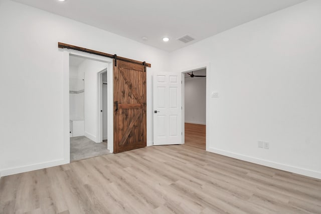 unfurnished bedroom featuring a barn door, a walk in closet, a closet, and light hardwood / wood-style floors