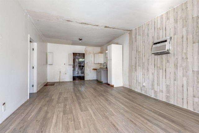 unfurnished living room with light hardwood / wood-style floors, an AC wall unit, and sink