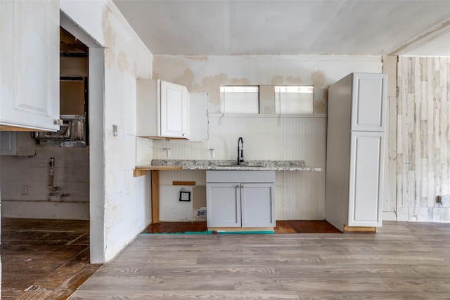 kitchen with light wood-type flooring, sink, light stone counters, and white cabinetry