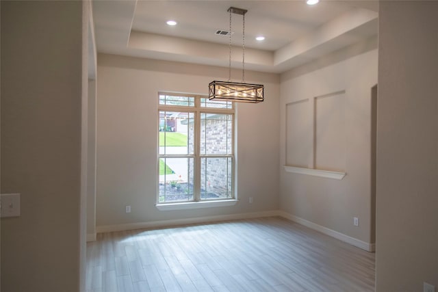 unfurnished room with a raised ceiling, light wood-type flooring, and a chandelier