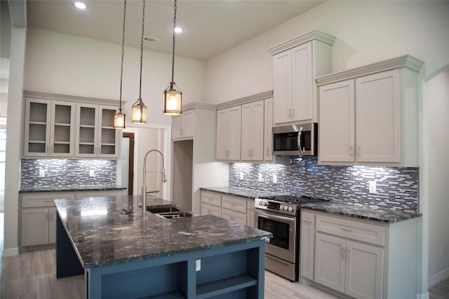 kitchen with sink, dark stone countertops, an island with sink, appliances with stainless steel finishes, and decorative light fixtures