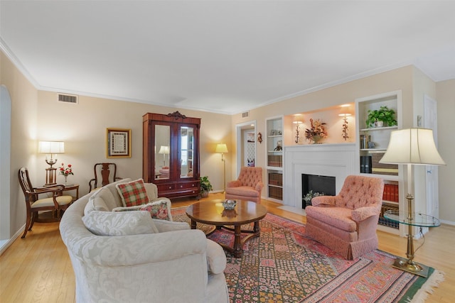 living room with light wood-type flooring, built in features, and crown molding