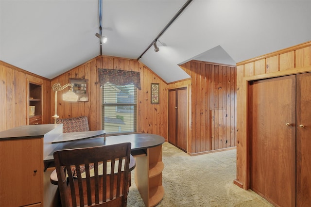 dining area with track lighting, vaulted ceiling, light colored carpet, and wood walls