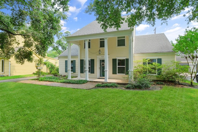 view of front of home with a shingled roof, a front yard, and covered porch