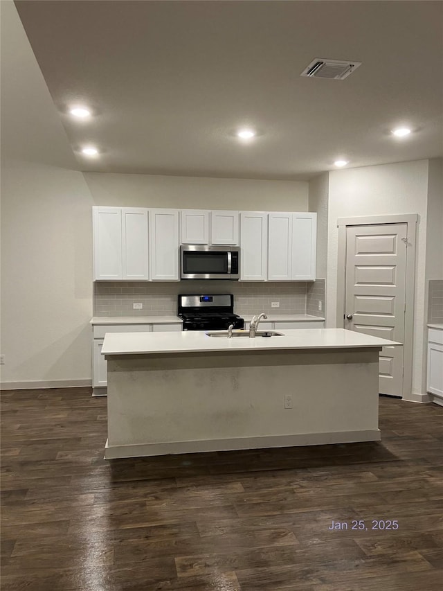 kitchen with an island with sink, appliances with stainless steel finishes, dark wood-type flooring, and white cabinets