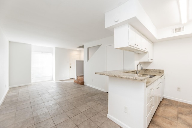 kitchen with kitchen peninsula, light stone countertops, white cabinetry, and sink