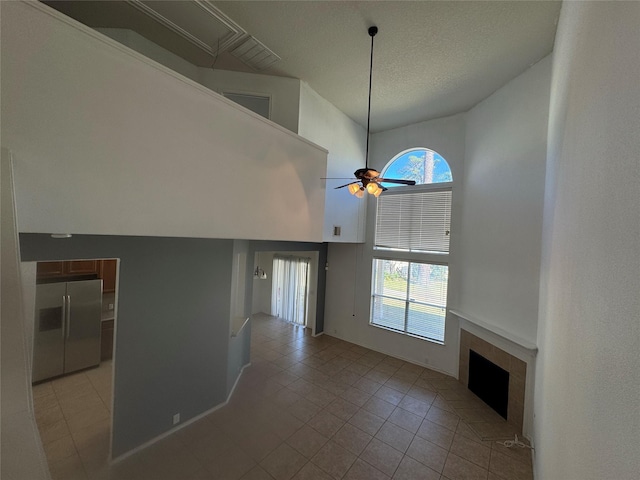 unfurnished living room featuring light tile patterned floors, a high ceiling, a healthy amount of sunlight, and a tiled fireplace