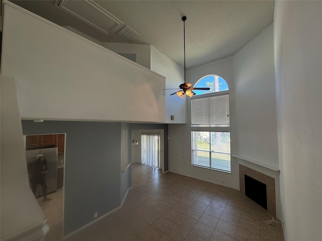 unfurnished living room featuring ceiling fan, light tile patterned floors, a fireplace, and a towering ceiling