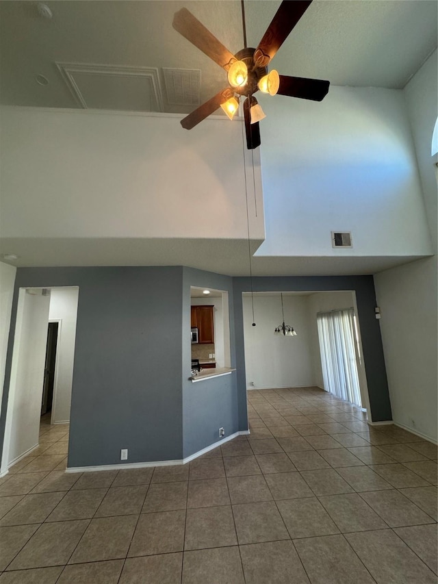 unfurnished living room with tile patterned flooring, a high ceiling, and ceiling fan with notable chandelier