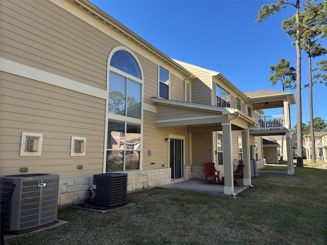 back of property with a balcony, a lawn, and central air condition unit