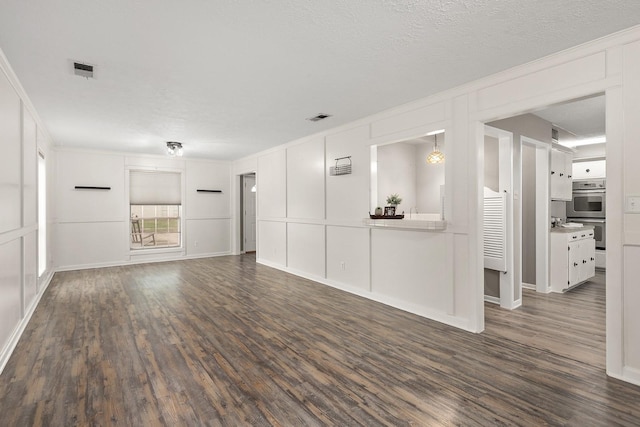 unfurnished living room with a textured ceiling, dark hardwood / wood-style floors, and ornamental molding