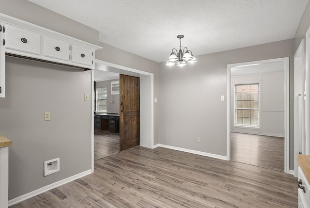 unfurnished dining area featuring a chandelier, light hardwood / wood-style floors, and a textured ceiling