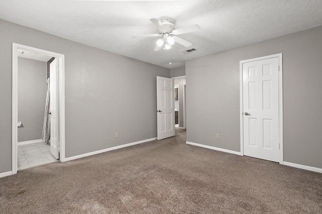 unfurnished bedroom featuring a textured ceiling, ceiling fan, light carpet, and ensuite bath