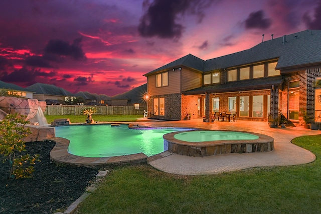 pool at dusk featuring an in ground hot tub, a patio, and a lawn