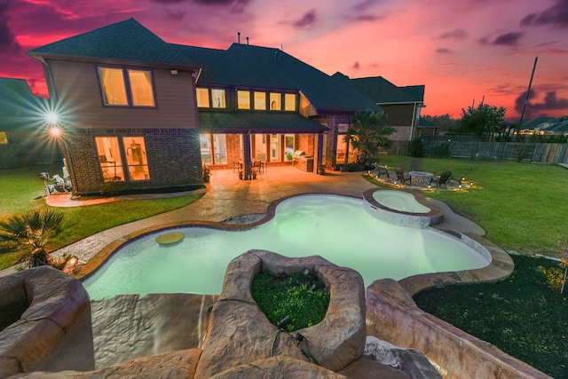 back house at dusk with a yard, a patio, and a swimming pool with hot tub