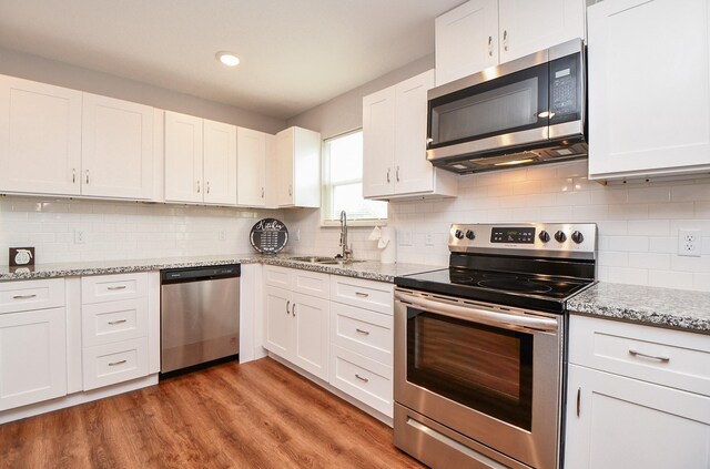 kitchen featuring decorative backsplash, appliances with stainless steel finishes, sink, white cabinets, and light hardwood / wood-style floors