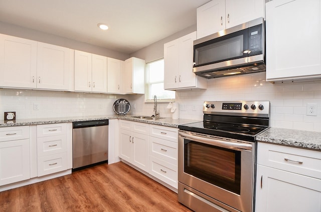 kitchen with white cabinets, appliances with stainless steel finishes, light stone countertops, light wood-type flooring, and a sink