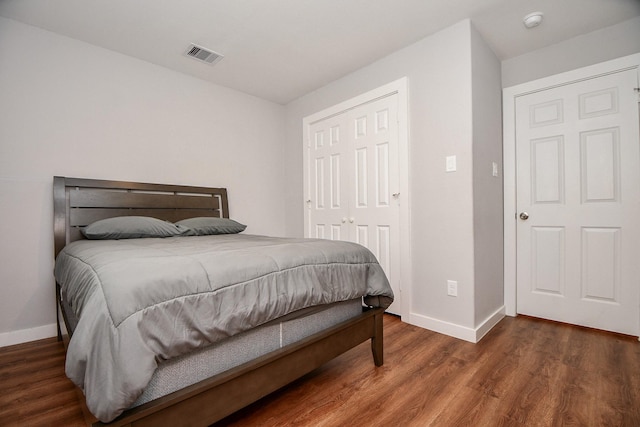 bedroom with a closet, wood finished floors, visible vents, and baseboards