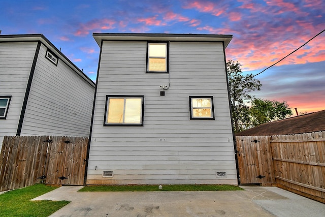 back of property at dusk with crawl space, fence, and a gate