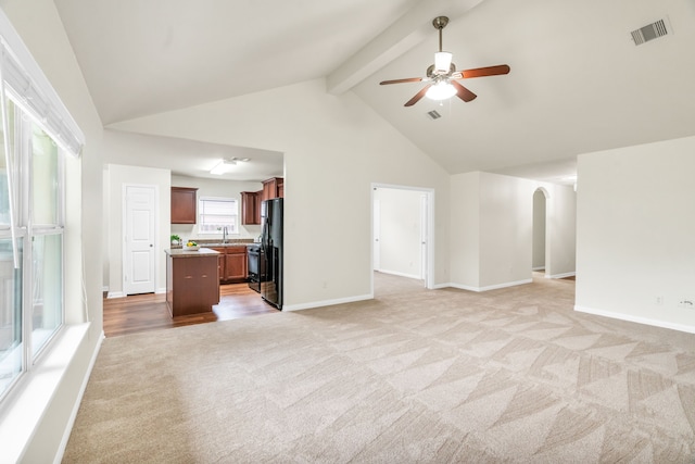 unfurnished living room featuring light carpet, high vaulted ceiling, sink, ceiling fan, and beamed ceiling