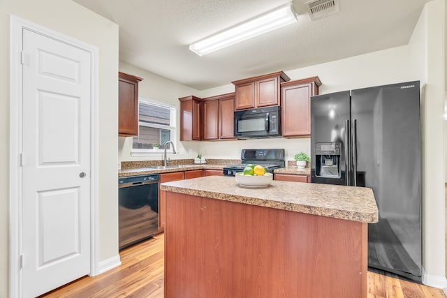 kitchen with black appliances, a kitchen island, light wood-type flooring, and sink