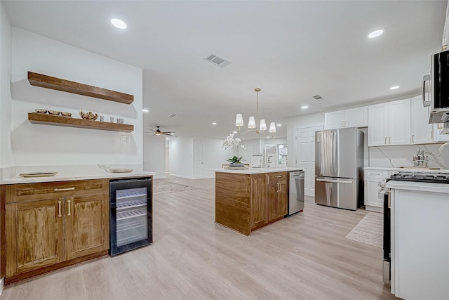 kitchen with a center island, beverage cooler, stainless steel appliances, pendant lighting, and white cabinets