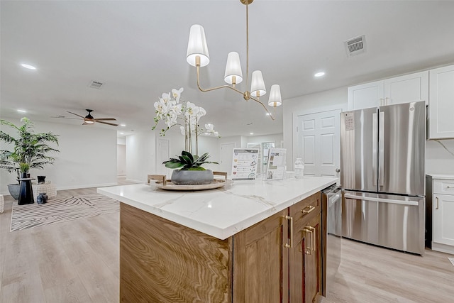 kitchen featuring light stone counters, decorative light fixtures, white cabinets, a center island, and stainless steel refrigerator