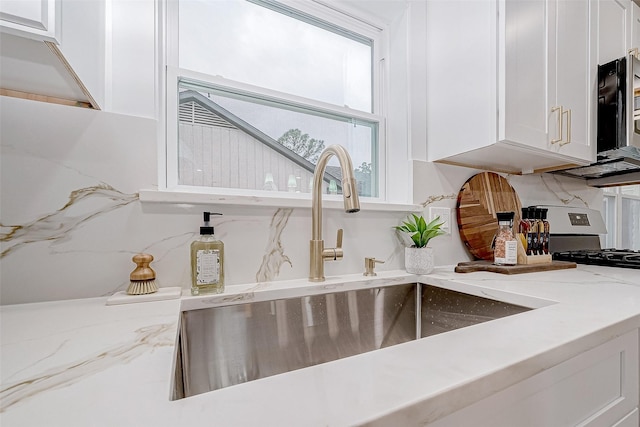 kitchen with gas range oven, white cabinetry, light stone countertops, and sink