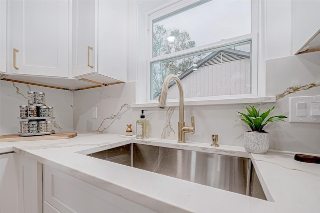 kitchen featuring decorative backsplash, light stone counters, white cabinetry, and sink