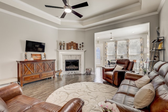 living room featuring a tray ceiling, a fireplace, ceiling fan, and light hardwood / wood-style flooring