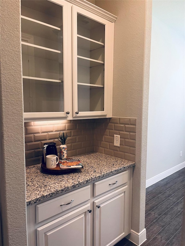 bar with backsplash, light stone countertops, and white cabinets