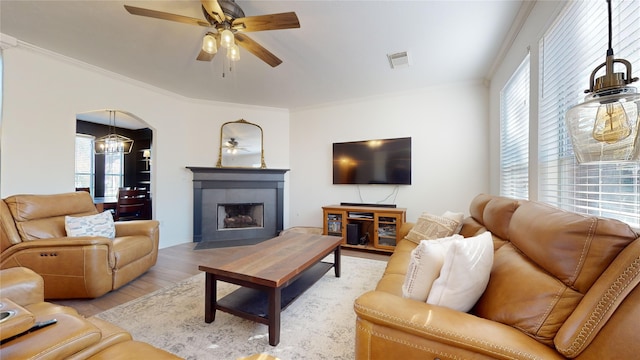 living room with a tiled fireplace, crown molding, light hardwood / wood-style flooring, and ceiling fan with notable chandelier