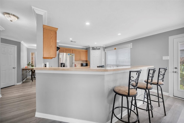 kitchen with stainless steel fridge with ice dispenser, light hardwood / wood-style flooring, kitchen peninsula, light brown cabinetry, and ornamental molding