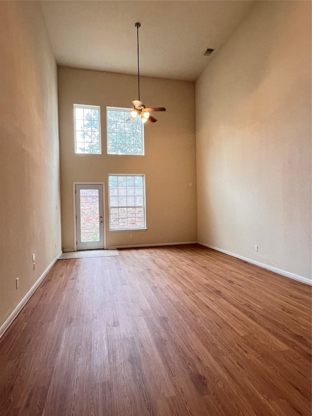 unfurnished room featuring hardwood / wood-style floors, a towering ceiling, and ceiling fan