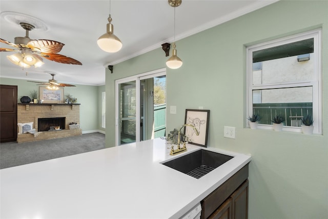 kitchen with pendant lighting, sink, a brick fireplace, ceiling fan, and ornamental molding