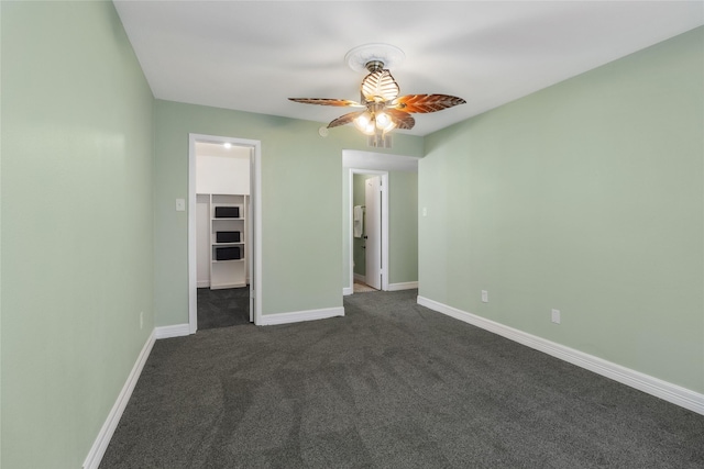 unfurnished bedroom featuring dark carpet, a closet, a spacious closet, and ceiling fan