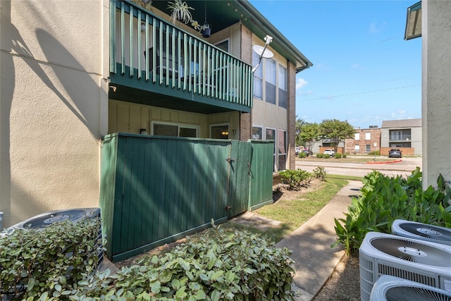 view of home's exterior featuring a balcony, fence, stucco siding, and central AC unit