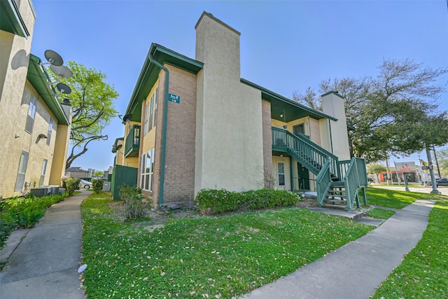 view of side of home featuring a lawn, a chimney, stairway, and brick siding