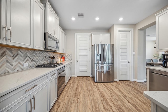 kitchen featuring stainless steel appliances, tasteful backsplash, light stone counters, light hardwood / wood-style floors, and white cabinets