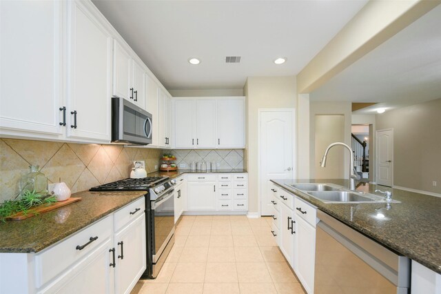 kitchen with sink, stainless steel appliances, light tile patterned floors, dark stone countertops, and white cabinets