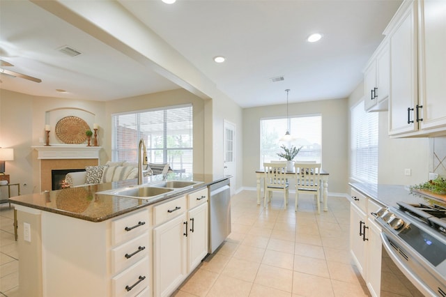 kitchen with sink, stainless steel appliances, dark stone counters, a center island with sink, and white cabinets