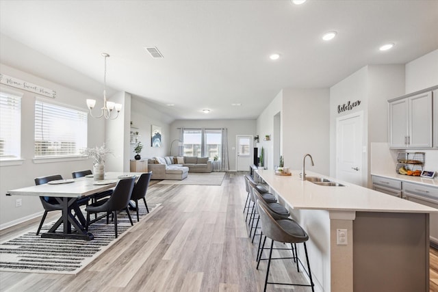 kitchen featuring gray cabinets, an island with sink, a breakfast bar area, and a chandelier