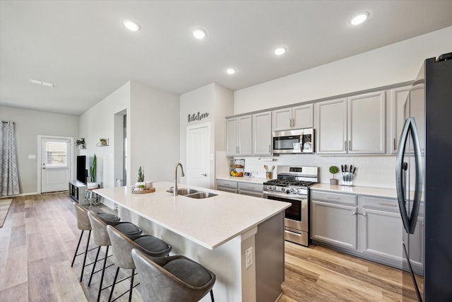 kitchen featuring sink, light wood-type flooring, a center island with sink, and appliances with stainless steel finishes