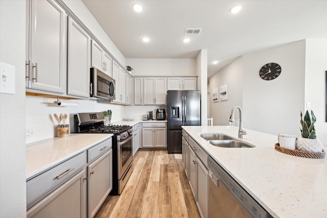 kitchen with appliances with stainless steel finishes, light stone counters, gray cabinetry, sink, and light hardwood / wood-style flooring