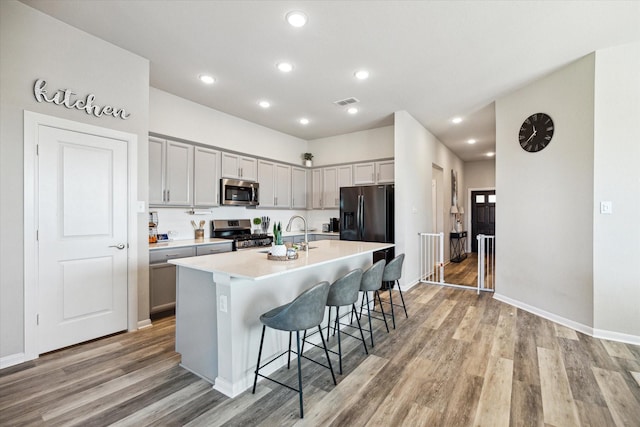 kitchen featuring stainless steel appliances, an island with sink, a breakfast bar area, gray cabinets, and light wood-type flooring