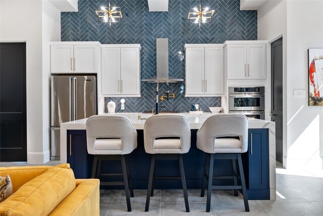 kitchen with wall chimney exhaust hood, white cabinetry, a kitchen island with sink, and appliances with stainless steel finishes