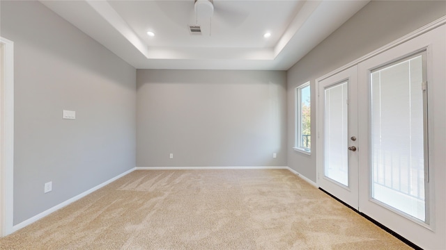 empty room featuring ceiling fan, a raised ceiling, light carpet, and french doors